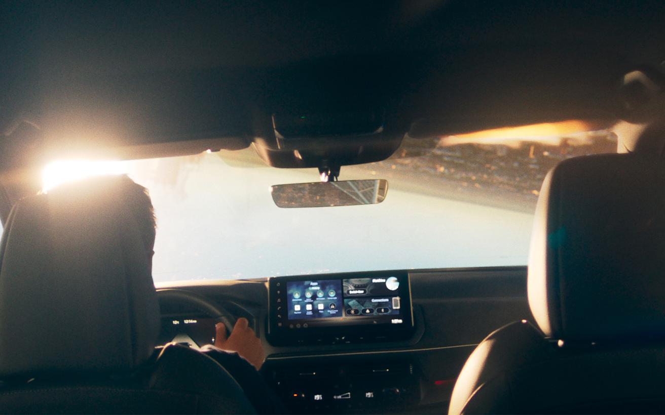 Innenraum eines Nissan Auto mit Blick auf das digitale Armaturenbrett und das Infotainment-System, Fahrer hält das Lenkrad.